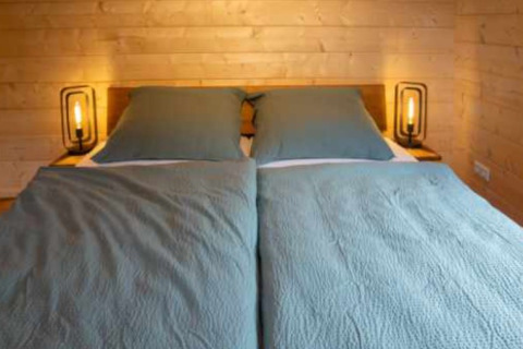 Letto matrimoniale con lenzuola blu e pareti in legno in una glamping di Natur-Camping Langenwald, Baden-Württemberg.
