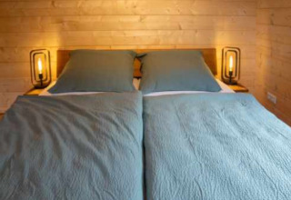 Double bed with blue linens and wooden walls in a Natur-Camping Langenwald glamping accommodation, Baden-Württemberg.