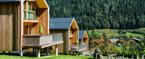 Træhytter med verandaer på grønne bakker, omgivet af skov i glampingstedet HOCHoben - Chalets Oostenrijk.