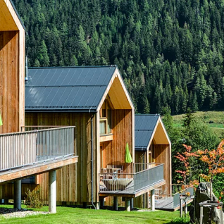 Træhytter med verandaer på grønne bakker, omgivet af skov i glampingstedet HOCHoben - Chalets Oostenrijk.