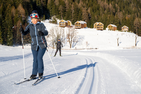 Due persone praticano sci di fondo vicino ai chalet in legno di HOCHoben - Chalets Oostenrijk, Austria innevata.