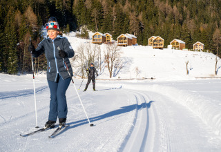 Due persone praticano sci di fondo vicino ai chalet in legno di HOCHoben - Chalets Oostenrijk, Austria innevata.