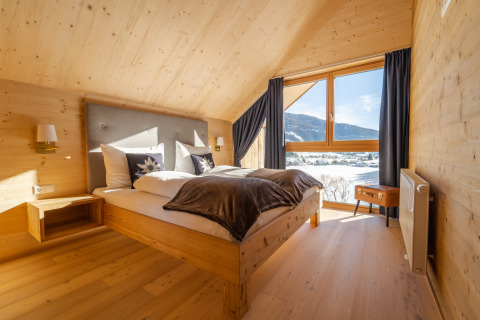 Hébergement glamping confortable avec chambre en bois, grande fenêtre, lit double et vue sur la montagne.