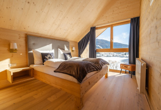 Hébergement glamping confortable avec chambre en bois, grande fenêtre, lit double et vue sur la montagne.