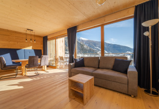 Comfortabele woonkamer in HOCHoben - Chalets Oostenrijk met grote ramen en prachtig uitzicht op besneeuwde bergen.
