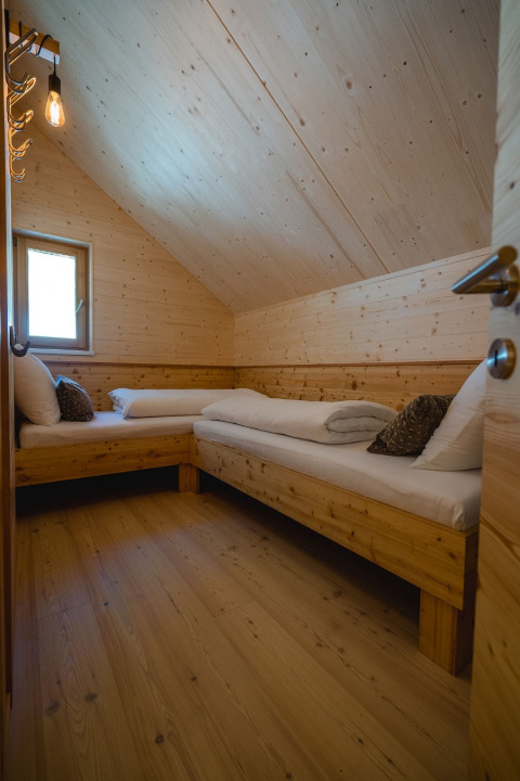 Gemütliches Glamping-Zimmer mit zwei Holzbänken und Dachschräge bei HOCHoben Chalets Österreich.