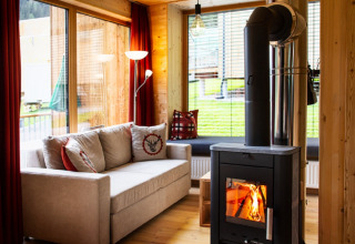 Gemütliches Wohnzimmer in HOCHoben - Chalets Österreich mit Sofa, Kamin und Panoramafenstern zur Natur.