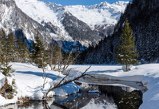 Paysage d’hiver aux HOCHoben - Chalets Oostenrijk avec montagnes enneigées, pins et lac reflétant la nature.