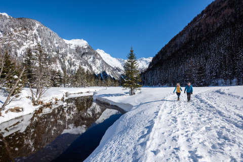 Due persone camminano lungo un sentiero innevato vicino a HOCHoben - Chalets Oostenrijk, tra le montagne.