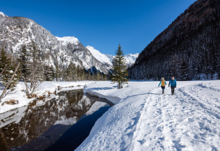 Zwei Menschen wandern im verschneiten Tal bei HOCHoben - Chalets Oostenrijk, flankiert von Bergen und Fluss.