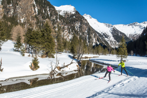 Due persone fanno sci di fondo accanto a un fiume tra le montagne innevate presso HOCHoben - Chalets Oostenrijk.