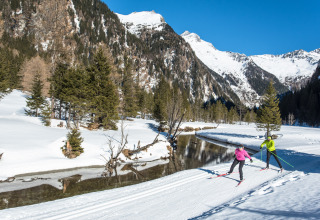 Twee personen langlaufen langs een rivier in een besneeuwde bergomgeving bij HOCHoben - Chalets Oostenrijk.