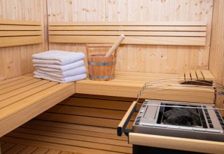 Intérieur d’un sauna avec bancs en bois, serviettes, seau et poêle chez HOCHoben - Chalets Oostenrijk glamping.