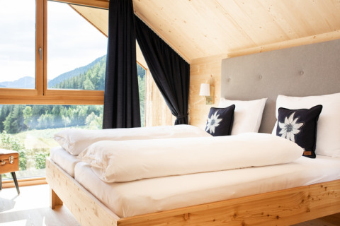 Bright bedroom at HOCHoben - Chalets Oostenrijk with modern wood design and scenic mountain window view.