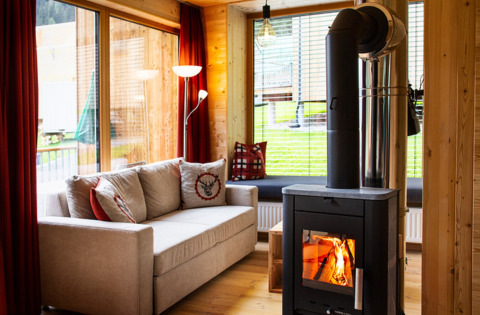 Hygge glampingophold i HOCHoben Chalets, Østrig, med sofa, trævægge, pejseovn og store vinduer til udsigt.