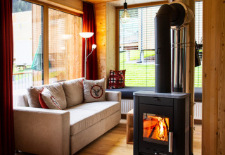 Hygge glampingophold i HOCHoben Chalets, Østrig, med sofa, trævægge, pejseovn og store vinduer til udsigt.