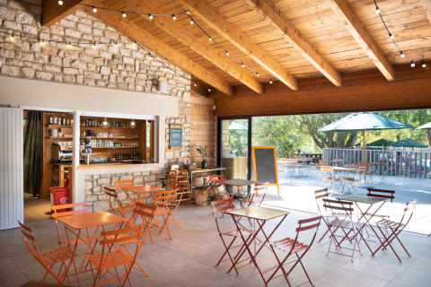 Hyggelig café med trætag og stenmure på Huttopia Le Moulin - Glamping Ardèche, udendørs siddepladser synlige.