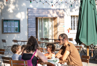 Family enjoying a meal outside at Huttopia Le Moulin - Glamping Ardèche under colorful string lights.