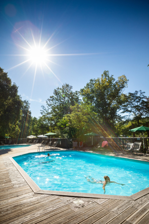 Giornata soleggiata in piscina a Huttopia Le Moulin - Glamping Ardèche, circondata da alberi e lettini.