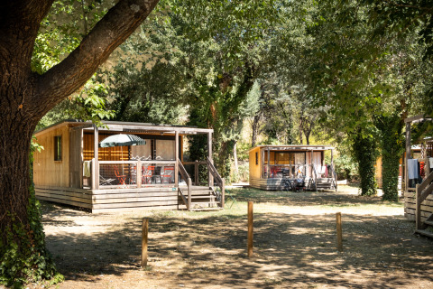 Alojamientos glamping de madera entre árboles en Huttopia Le Moulin - Glamping Ardèche, Francia.