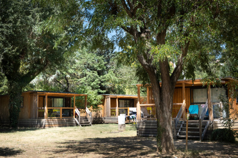 Glamping-Unterkünfte im Huttopia Le Moulin - Glamping Ardèche, umgeben von Bäumen und Natur im Sommer.