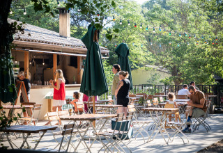 Outdoor café area at Huttopia Le Moulin - Glamping Ardèche with guests at tables under trees and string lights.