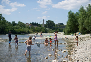 Des gens profitent d'une journée ensoleillée au bord de la rivière à Huttopia Le Moulin - Glamping Ardèche.