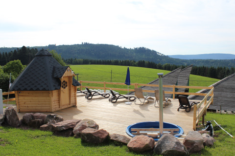 Glamping pod on a wooden deck, lounge chairs, and scenic views of green hills in the Black Forest, Germany.