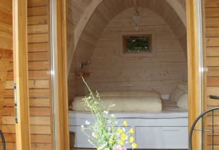 Ingresso di un’accogliente pod di legno con letto, tavolo e fiori, glamping Äckerhof nella Foresta Nera.