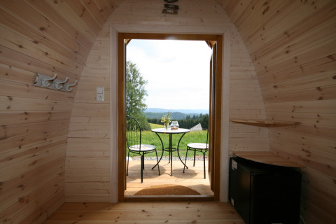 Vue intérieure d'une cabane en bois s'ouvrant sur une terrasse avec table, chaises et vue naturelle.