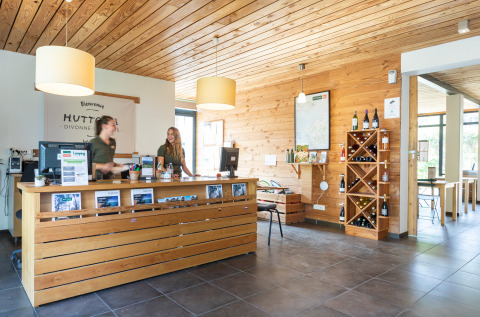 Réception des Huttopia Winter Chalets – Divonne Les Bains avec décor en bois et personnel accueillant pour le glamping.