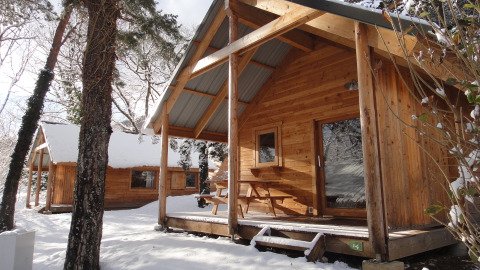 Chalets en bois sous la neige à Huttopia Winter Chalets, Divonne Les Bains, glamping dans les Alpes françaises.