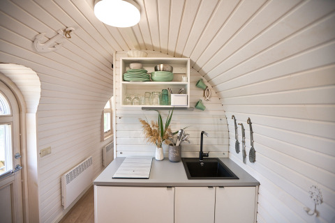 Acogedora y luminosa cocina de glamping en una cabaña iglú, con estantes abiertos, vajilla y fregadero.