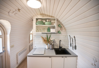Sfeervolle, lichte keuken in een glamping iglohut met open rekken, servies en een spoelbak.
