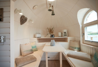 Gezellig interieur van glamping iglohut in Iglu Camp Tangermünde met zitbank, tafel en venster.