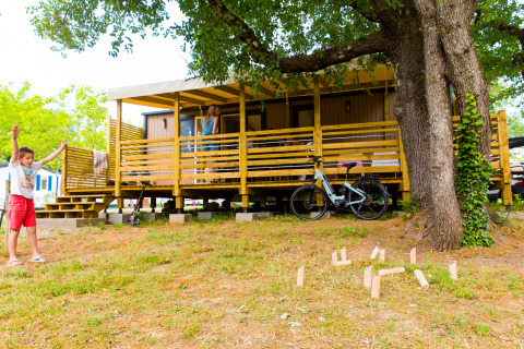 Bambino che gioca davanti a una cabina glamping in legno presso Camping La Chapoulière - Glamping Ardèche.