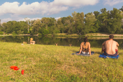 Personas descansando junto a un río con árboles al fondo en Camping La Chapoulière - Glamping Ardèche.