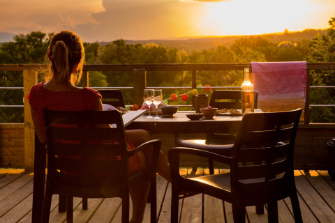 Frau genießt den Sonnenuntergang mit Wein auf der Terrasse von Camping La Chapoulière - Glamping Ardèche.