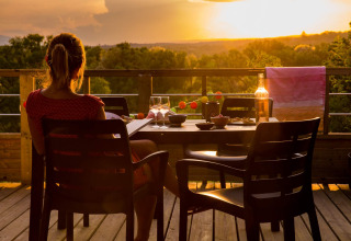 Donna che si gode il tramonto con un bicchiere di vino sulla terrazza di Camping La Chapoulière - Glamping Ardèche.