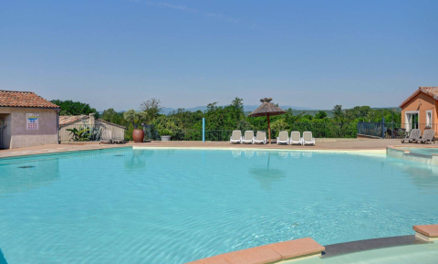 Udendørs swimmingpool med liggestole og udsigt til grønne bakker på Camping La Chapoulière, Ardèche, Frankrig.