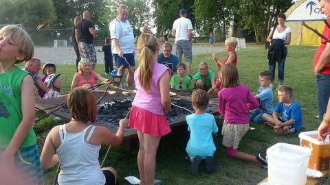 Bambini e adulti si riuniscono intorno a un falò al Campingpark Rerik - Glamping Rerik, godendo insieme la natura.