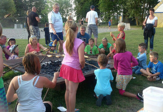 Children and adults gather around a campfire at Campingpark Rerik - Glamping Rerik, enjoying outdoor fun together.