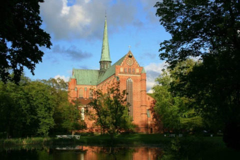 Red brick church with tall spire surrounded by trees near Campingpark Rerik - Glamping Rerik by water.