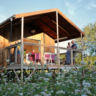 Dihan Evasion - Lodges Bretagne: mensen ontspannen op een houten veranda met bloemenweide op de voorgrond.