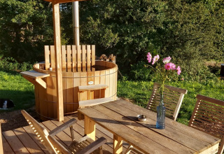 Houten terras bij Dihan Evasion, Bretagne, met hot tub, tafel, stoelen en bloemen, omringd door natuur.