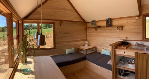 Alojamiento glamping moderno con interior de madera, sofá esquinero, cocina y grandes ventanas al exterior.