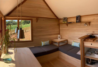 Modern lodge di glamping con interni in legno, divano angolare, cucina e grandi finestre sulla natura.