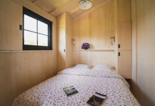 Cozy wooden bedroom with double bed, floral bedding and window at Dihan Evasion - Lodges Bretagne.
