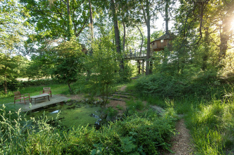 Baumhaus mit Terrasse und Sitzbereich am Teich im Grünen bei Dihan Evasion - Lodges Bretagne Glamping-Unterkunft.