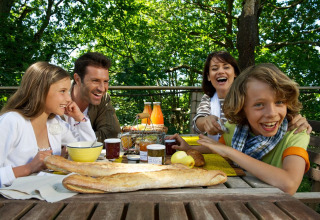A family enjoys breakfast outside at Dihan Evasion - Lodges Bretagne with baguette, juice, and jam.